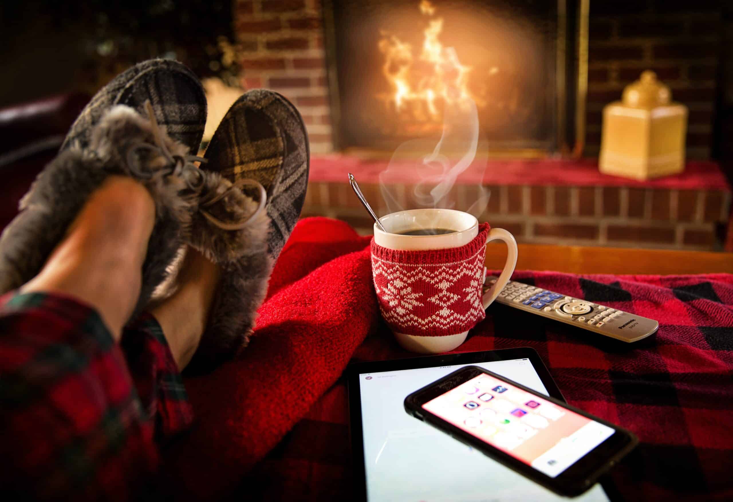 person wearing slippers with a hot coffee by a fire