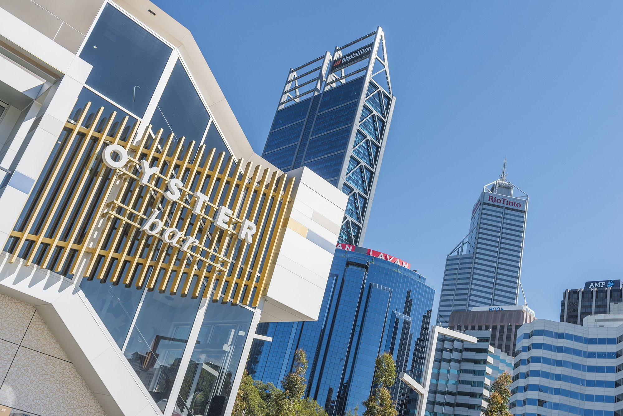 A modern Oyster Bar building with wooden accents, set against a backdrop of iconic city skyscrapers under a clear blue sky.